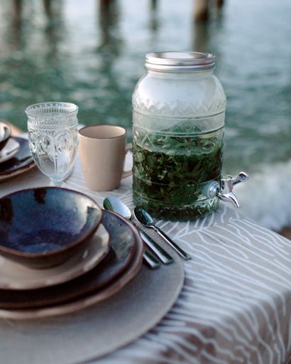 A glass container of drink next to dish set on background of waters