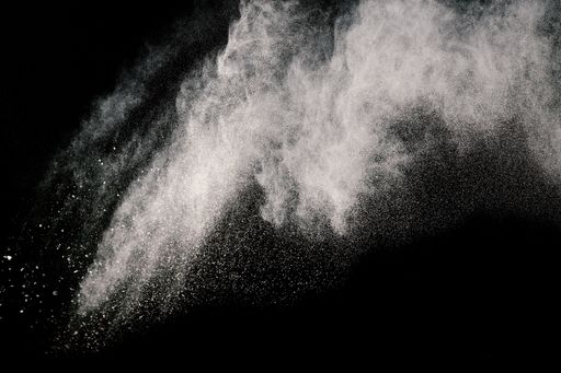 A grayscale of some brown particles exploding on black background, brown dust splashing