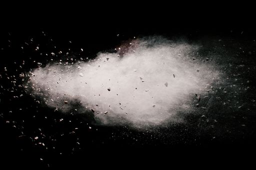 A grayscale of some brown particles exploding on black background, brown dust splashing