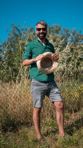 A vertical shot of an attractive middle-aged male holding a straw hat and smiling in a field