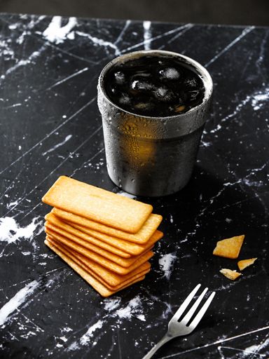 A vertical shot of crackers and a steel cup with ice on a granite surface table