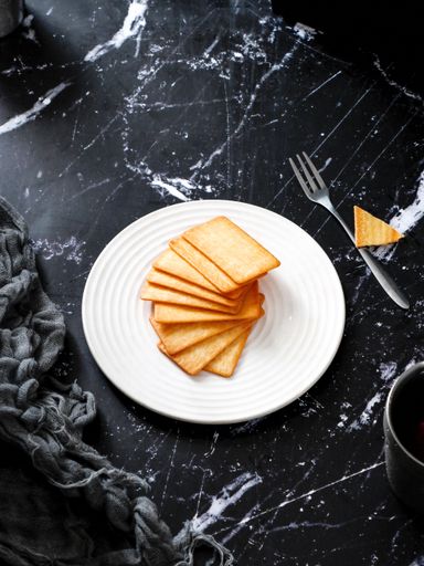 A vertical shot of crackers in a white plate on a granite surface table