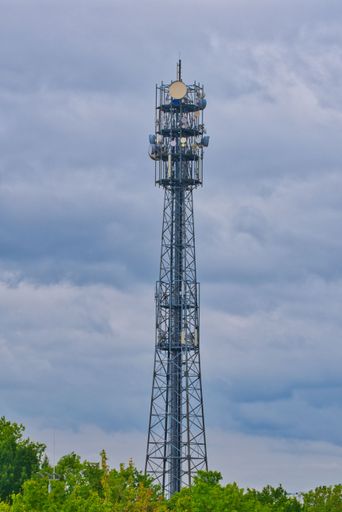 A telecommunications tower with many antennas, steel structure tower and blue cloudy sky