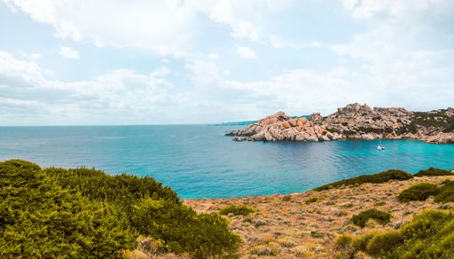 A panoramic view of the island bay out of stone and rocks with small boat in it on cloudy summer day