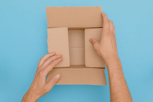 A top view of hands fold empty cardboard box ready to deliver as package on blue background