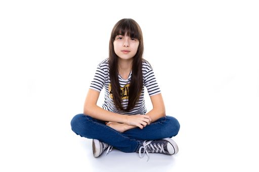 A beautiful 10 year old girl sitting with crossed legs on floor while crossing arms and look serious and straight into camera
