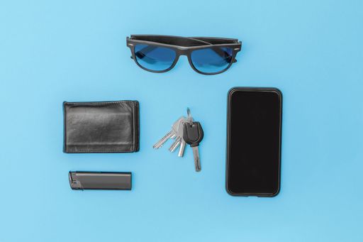 Top view of modern man items, on table cell phone sunglasses lighter wallet keys in black on blue background