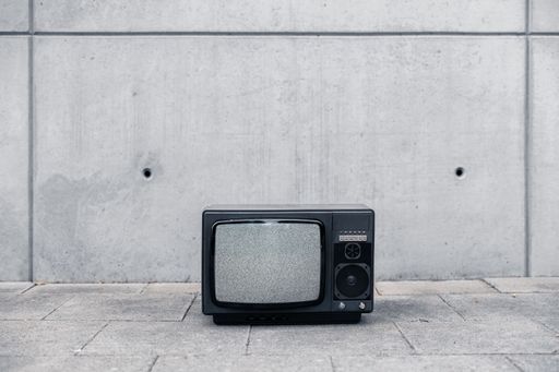 An old retro tv stand outside on street in front of grungy concrete wall without signal on screen only noise
