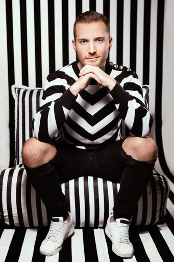 A vertical of a sitting man on a chair with fingers crossed and looking at the camera with a little smile on his lips