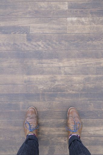 A top view of a person wearing brown Brogue shoes and standing on a wooden floor