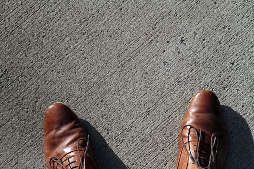 A top view of a person wearing brown Oxford shoes and standing on a rough surface under the sunlight