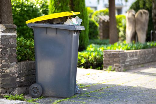 A full garbage trash standing at sidewalk next to street