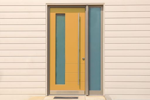 A yellow front door on wooden wall with glass and long metal handle