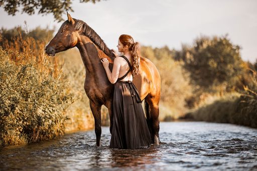 A woman and young horse standing in water next to each other enjoying the summer