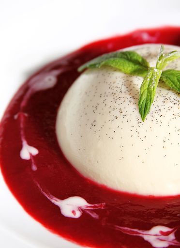 An aesthetic vertical closeup shot of a Panna cota with red sauce and mint