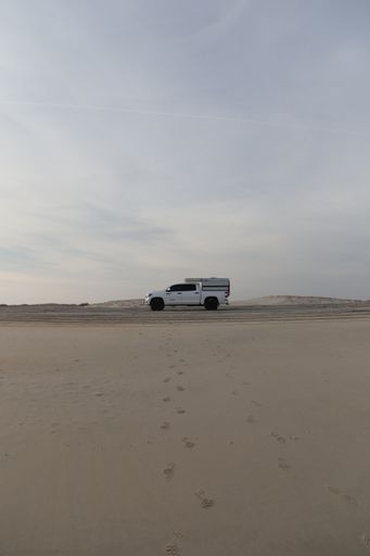 A vertical shot of footsteps on the sand in a deserted area leading to a white van