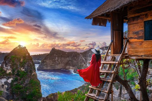 A female with a red the steps of a tree house at sunrise in Nusa Penida island, Bali, Indonesia
