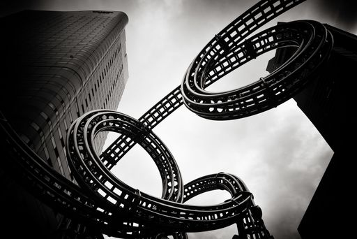 A greyscale shot of a high rise building next to an object designed to look like a film tape