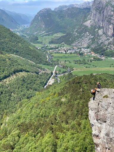 A vertical shot of a young woman sitting on the edge of a cliff and looking at mountains