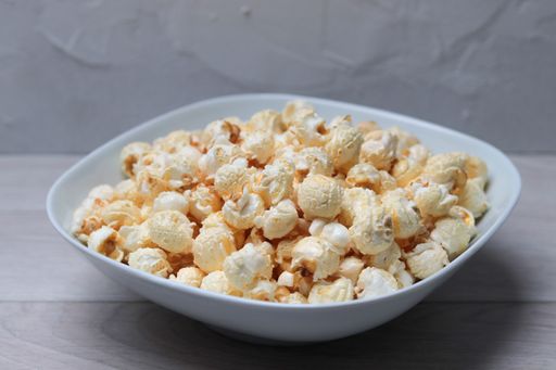 A closeup shot of popcorn in a white bowl on a white surface