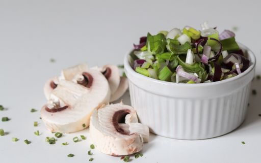 A closeup shot of a white bowl with vegetable salad and sliced mushrooms on a white surface