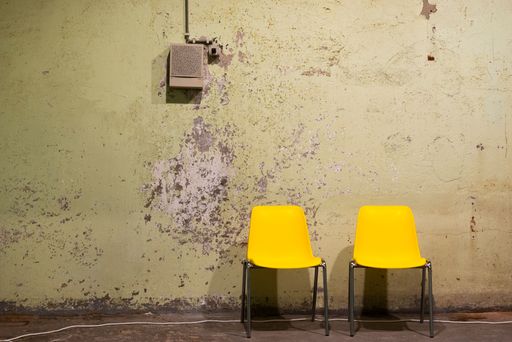 A pair of plastic yellow chairs near a broken wall