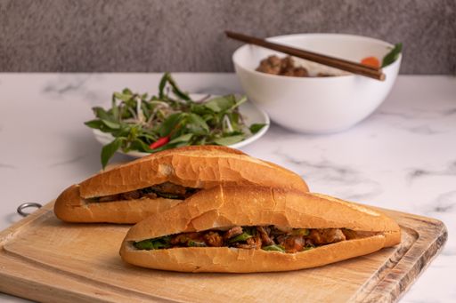 A high angle shot of banh mi, a Vietnamese pork sandwich on a cutting board on a marble surface