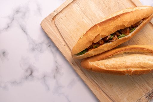 A high angle shot of banh mi, a Vietnamese pork sandwich on a cutting board on a marble surface