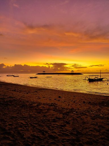 A vertical shot of boats moored at Sanur Beach, Bali near an island at beautiful sunset