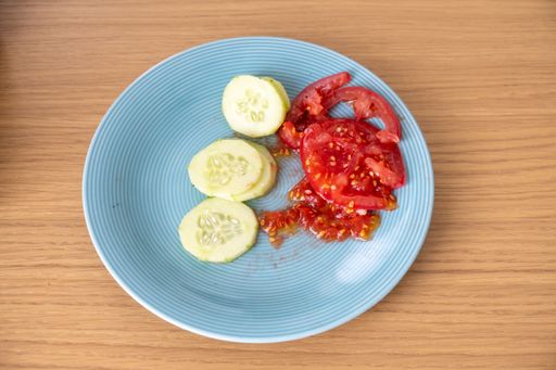 A top view of a blue plate with sliced cucumbers and tomatoes on a wooden surface