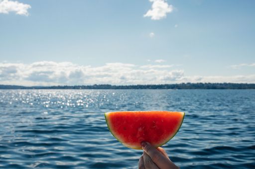 hand holding up watermelon semi moon, circle slice out on boat, lake