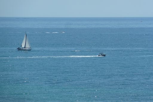 An aerial shot of a sailboat and a high-speed boat in blue sea under clear sky