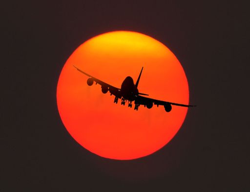 A beautiful shot of a plane in flight in front of the red sun