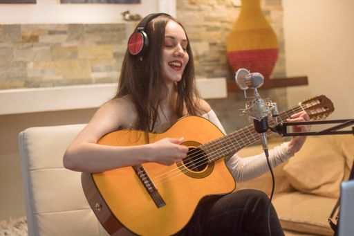 A closeup shot of a young female artist playing the guitar and singing while recording it