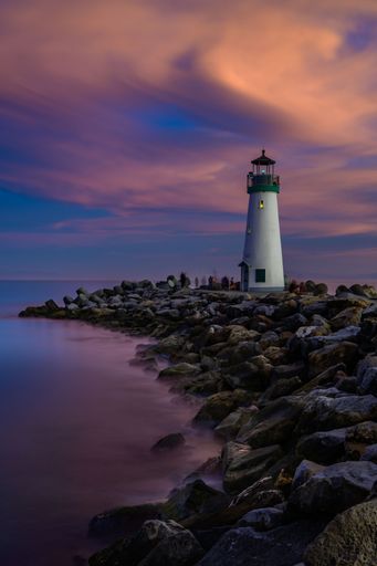 A breathtaking view of a lighthouse at the Walton beach under a colorful sunset sky