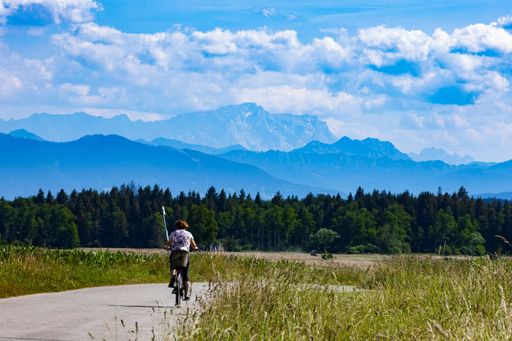 A cyclist on a road with green trees and blue mountain silhouettes in the background.