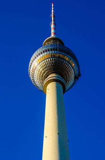 A vertical low angle shot of the top of the famous Fernsehturm tower in Berlin against the blue sky