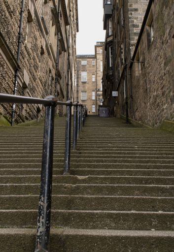 A vertical shot of stairs with a handrail leading up, between old stone buildings in Edinburgh, Scotland, UK