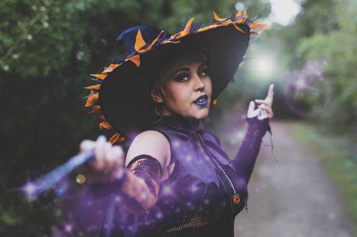 A woman wearing a witch makeup and costume with a decorated hat and holding a wand  - the concept of Halloween