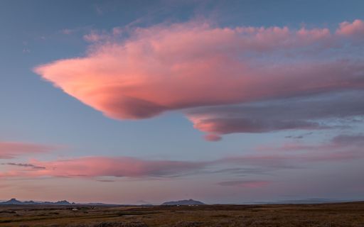 A big pink cloud in a sunset sky over a beautiful field with mountains in the background in Iceland