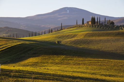 A beautiful shot of a country house in the middle of a field surrounded by hills under the clear sky