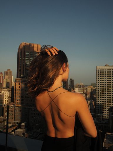 A vertical shot of a female standing in the wind looking out over a city