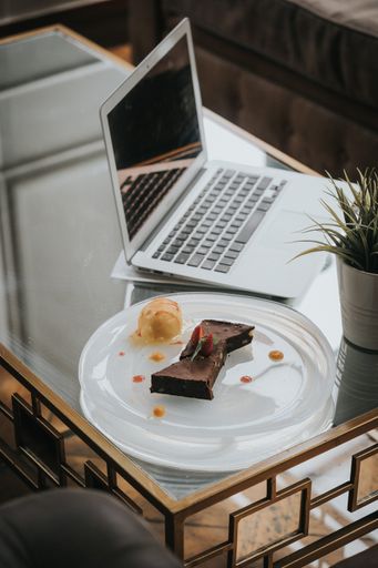 A vertical shot of fresh tasty chocolate cheesecake with a strawberry and a laptop on the table