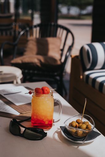 A vertical shot of green olives in a bowl on the table with a jar of iced berry lemonade on it