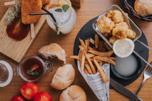 A top view of tasty chicken nuggets, French fries, bread, tomatoes on a wooden table