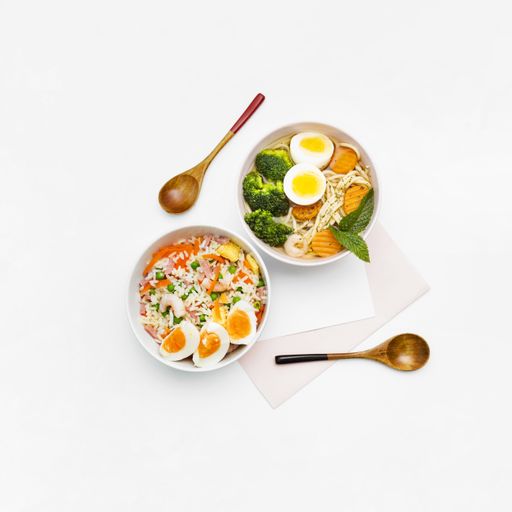 A top view of Asian food made with eggs, vegetables, noodles and other ingredients on a white background with copy space - great for menu use