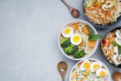 A top view of Asian food made with eggs, vegetables, noodles and other ingredients on a white background with copy space - great for menu use