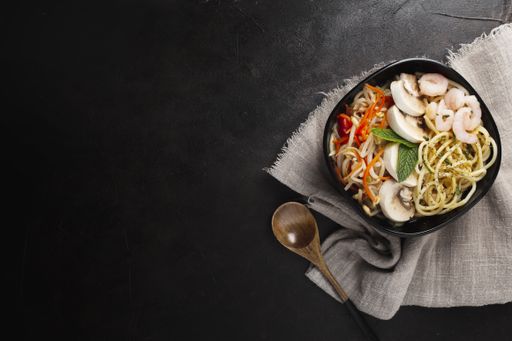 A closeup shot of asian food made with noodles, mushrooms, and vegetables on a black surface with copy space
