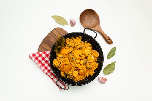 A closeup shot of delicious Spanish rice in a paella pan on a white surface with copy space - great for menu use