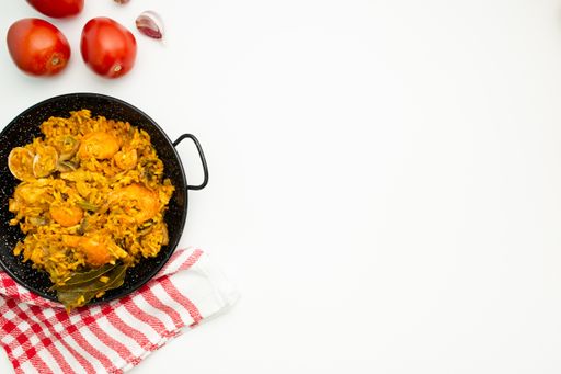 A closeup shot of delicious Spanish rice in a paella pan on a white surface with copy space - great for menu use